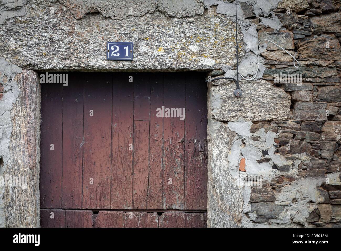 Rustikale rustikale spanische Holztür in einer abgenutzten verwitterten Steinwand mit der Nummer 21 über dem Rahmen gesetzt. Landhaus Bauernhaus rusic uneben. Stockfoto