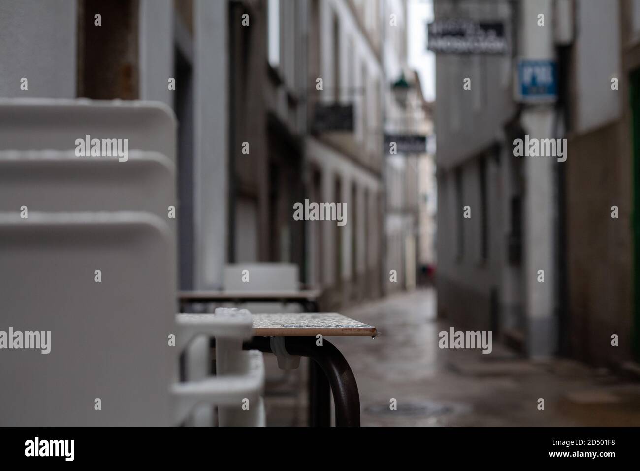 Gestapelte Plastikstühle aus einem Restaurant in einer alten rustikalen verregneten Straße von Santiago de Compostela, Spanien. Geschlossen gestapelt Tourismus spanien rustikal. Stockfoto
