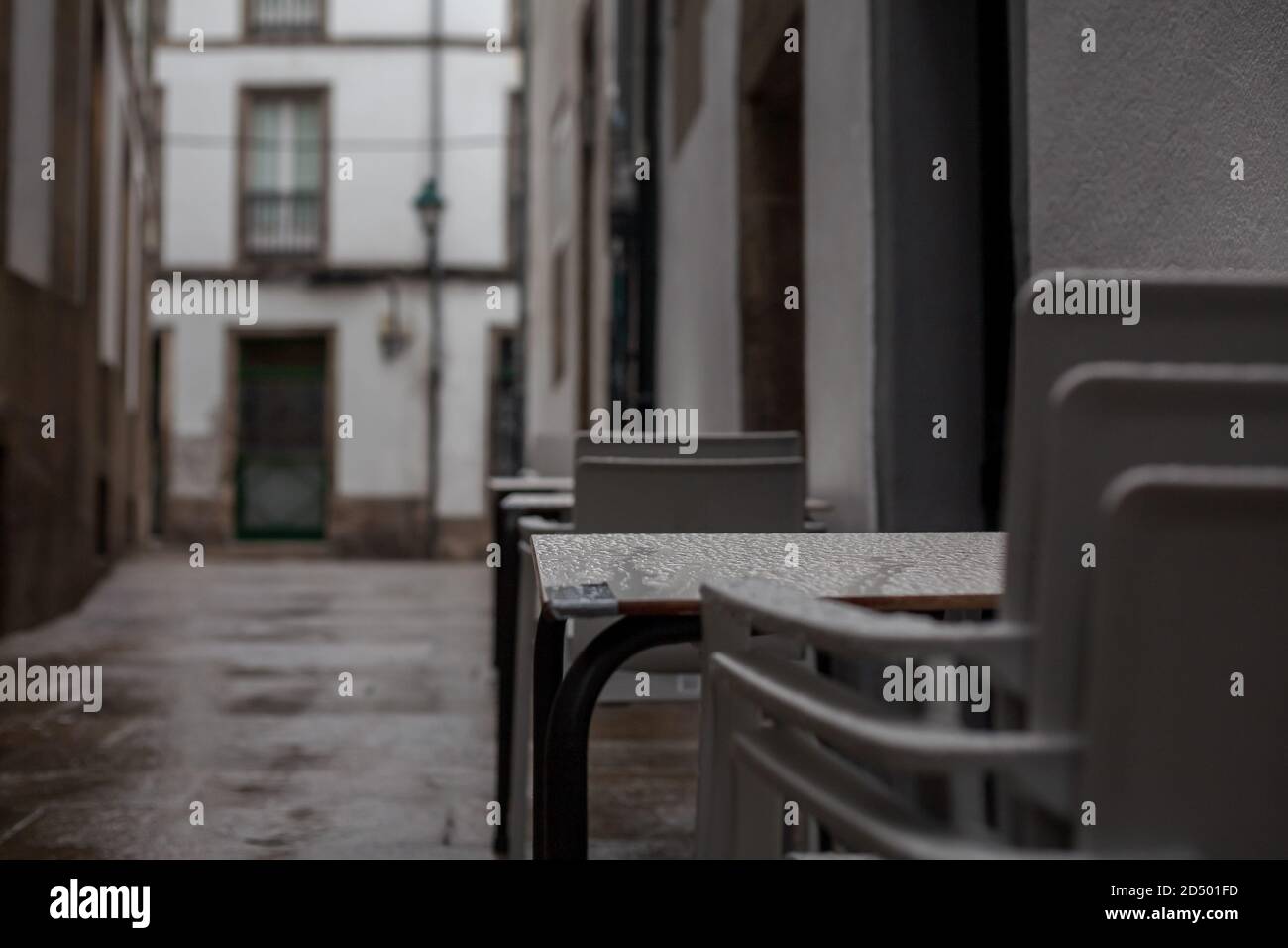 Gestapelte Plastikstühle aus einem Restaurant in einer alten rustikalen verregneten Straße von Santiago de Compostela, Spanien. Geschlossen gestapelt Tourismus Spanien rustikal. Stockfoto
