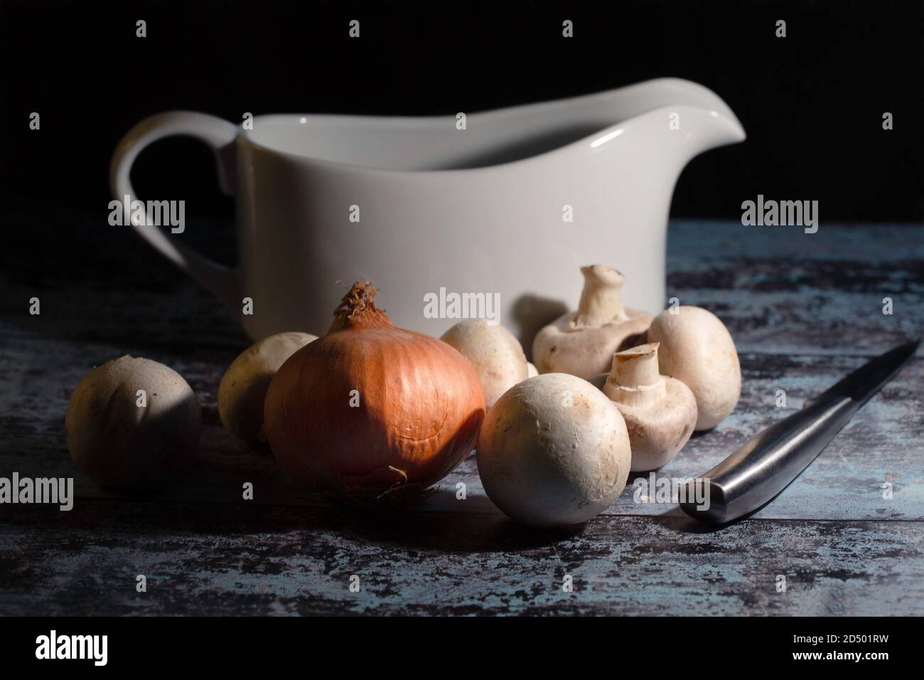 Stillleben Bild von rohen Pilzen, Zwiebel, Messer und Soße Boot über dunklen Hintergrund Stockfoto