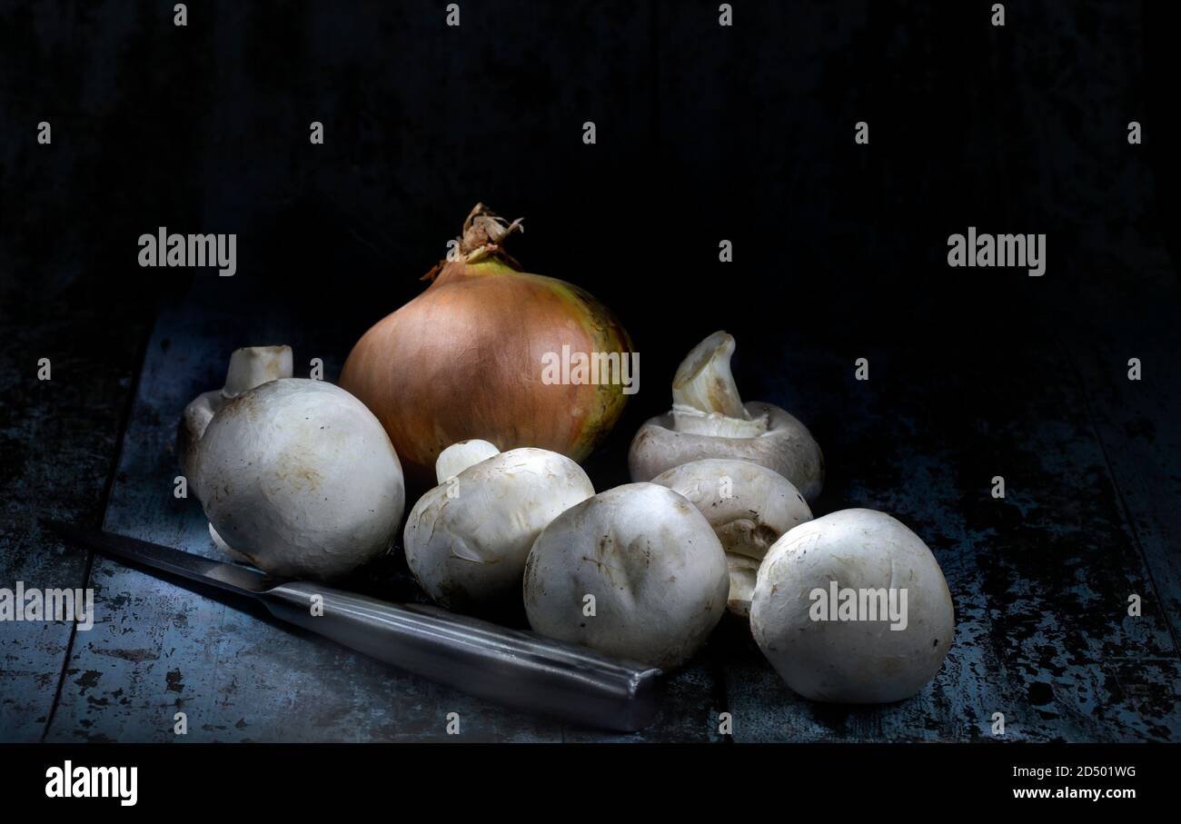 Stillleben Bild von rohen Pilzen, Zwiebel und Messer über dunklem Hintergrund Stockfoto