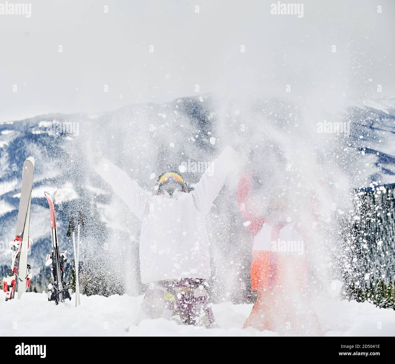 Zwei Skifahrer werfen frischen Pulverschnee hoch in die Luft. Mann und Frau haben Spaß im Skigebiet mit schönen Bergen im Hintergrund. Konzept der Wintersport-Aktivitäten, Spaß und Beziehungen. Stockfoto
