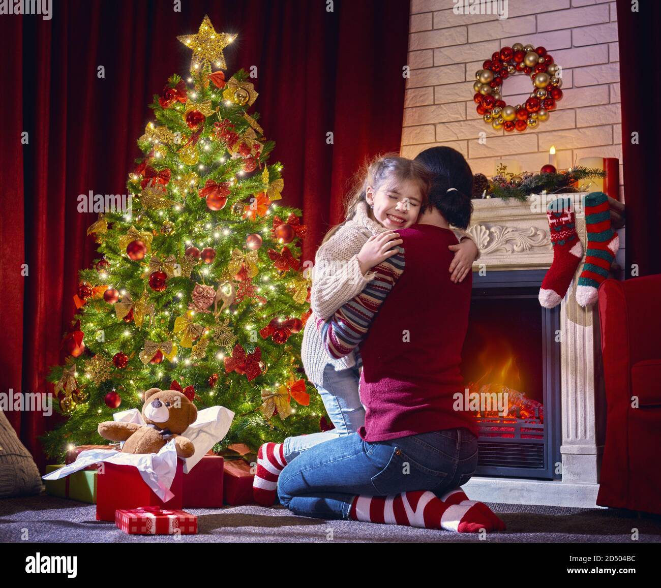 Frohe Weihnachten und schöne Feiertage! Nettes Kind Tochter Mädchen umarmt eine Mutter und ist froh, das Geschenk. Weihnachtstraditionen der Familie. Stockfoto