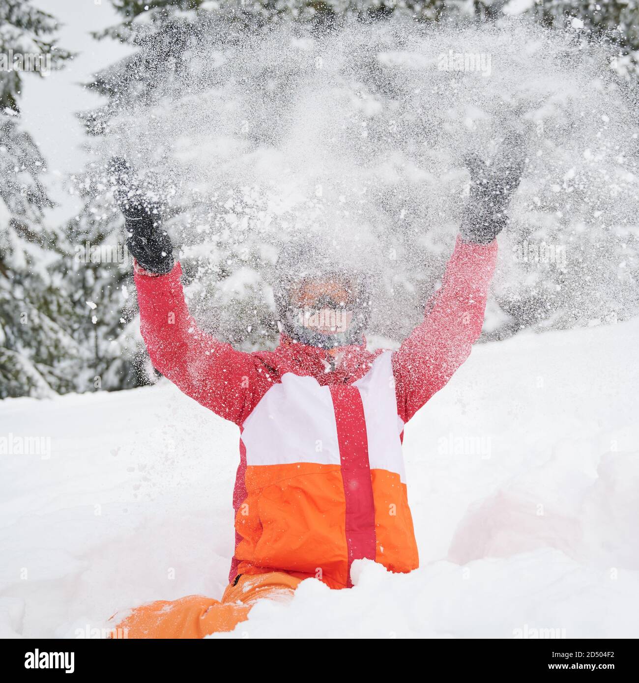 Glückliche Momente im Skigebiet in den Bergen. Frau im lebhaften Skikostüm sitzen und spielen mit Schnee, werfen es auf. Konzept der Winterunterhaltung Stockfoto