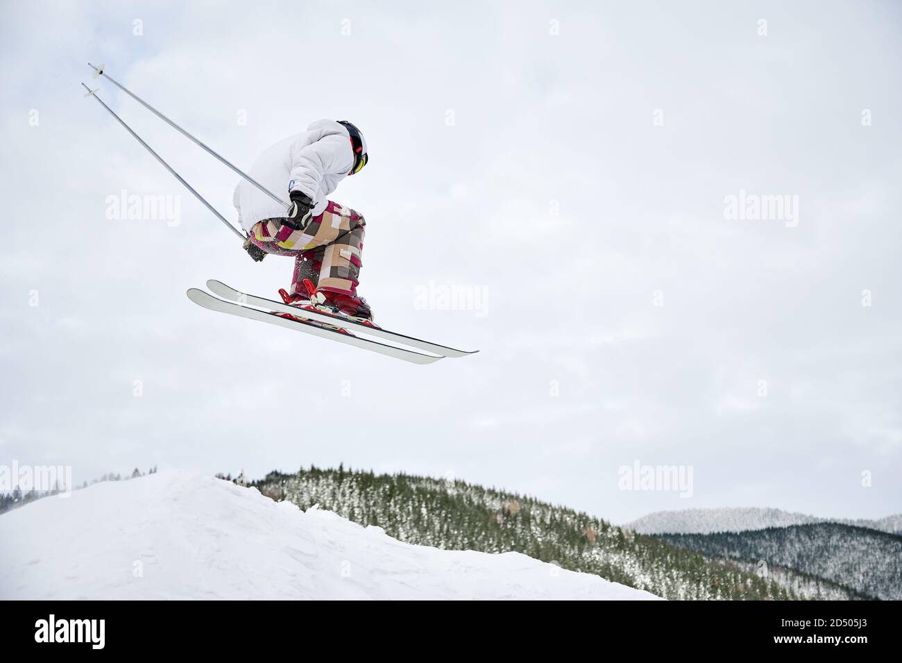Horizontale Momentaufnahme von spektakulären Freeriding-Fliegen an den steilen Hängen von Skifahrern. Cool Skisprung vom Hügel gegen bewölkten Himmel auf Hintergrund. Low-Angle-Ansicht, Kopierbereich. Extremes Sportkonzept Stockfoto