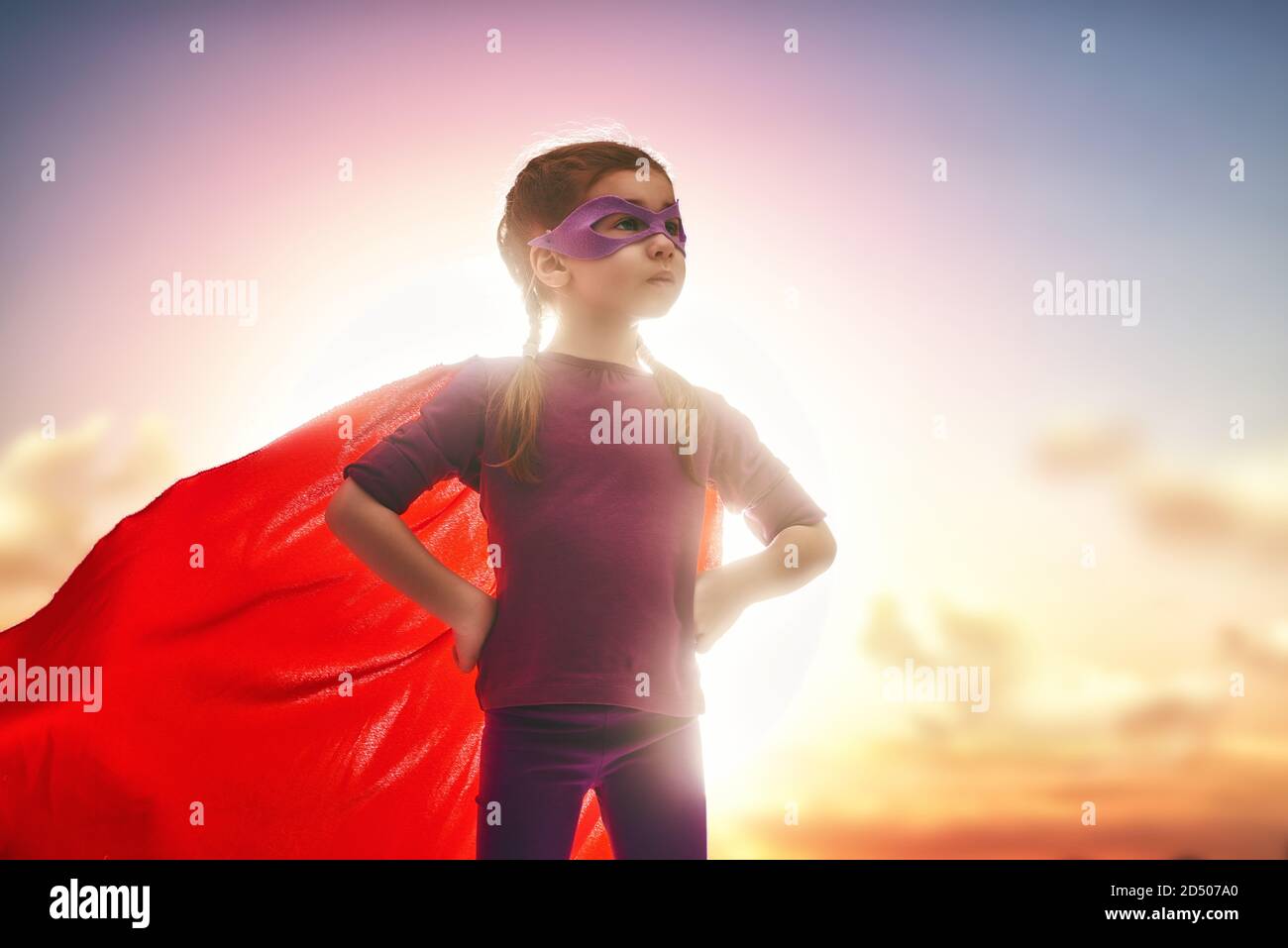 Kleines Mädchen spielt Superheld. Kind auf dem Hintergrund des Sonnenuntergangs Himmel. Mädchen Power Konzept Stockfoto
