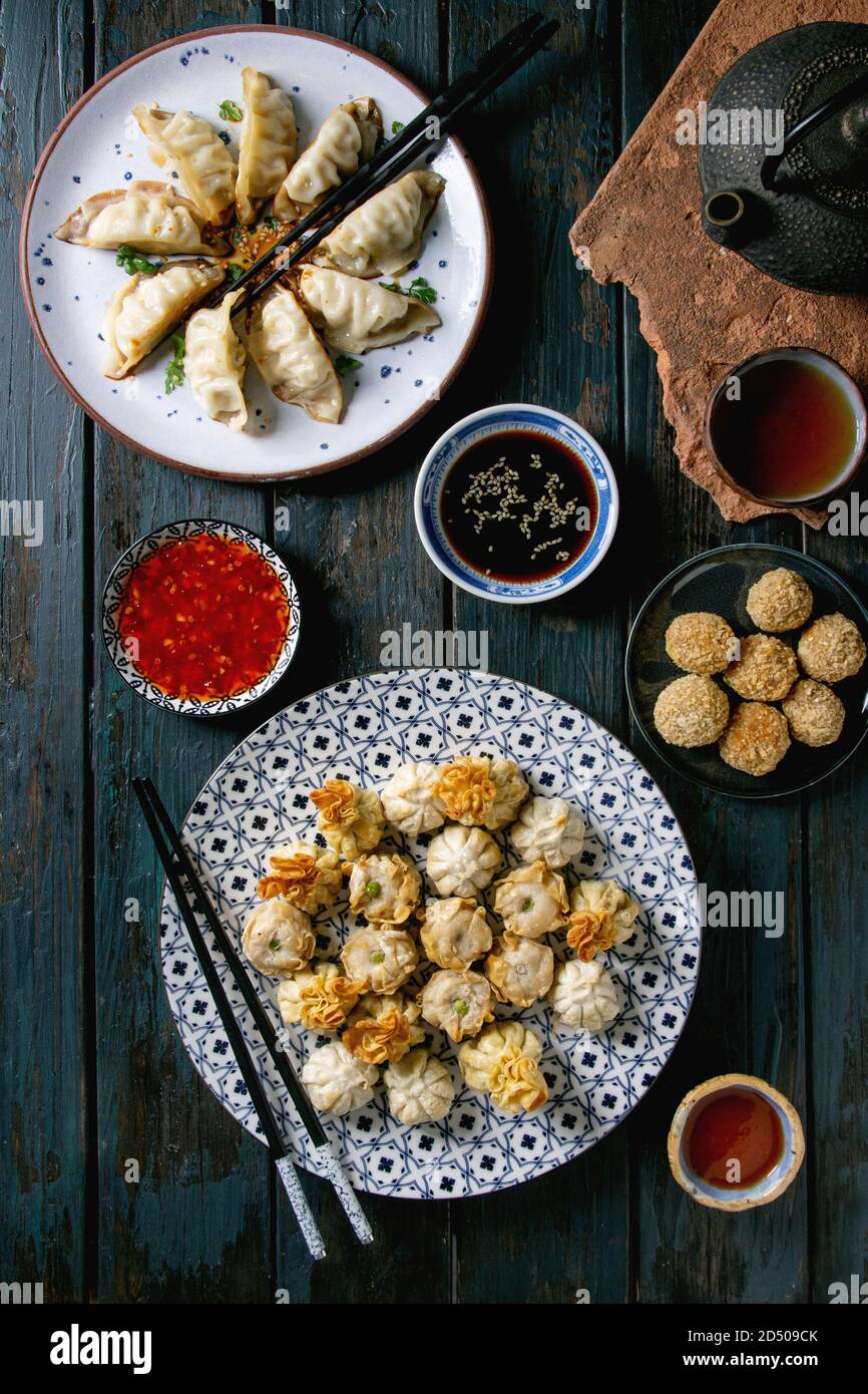 Dim Sum Gyozas asiatische gebratene Knödel Party mit verschiedenen Soßen in Keramik Teller serviert und Schüsseln mit Stäbchen, Teetassen und Teekanne über dar Stockfoto