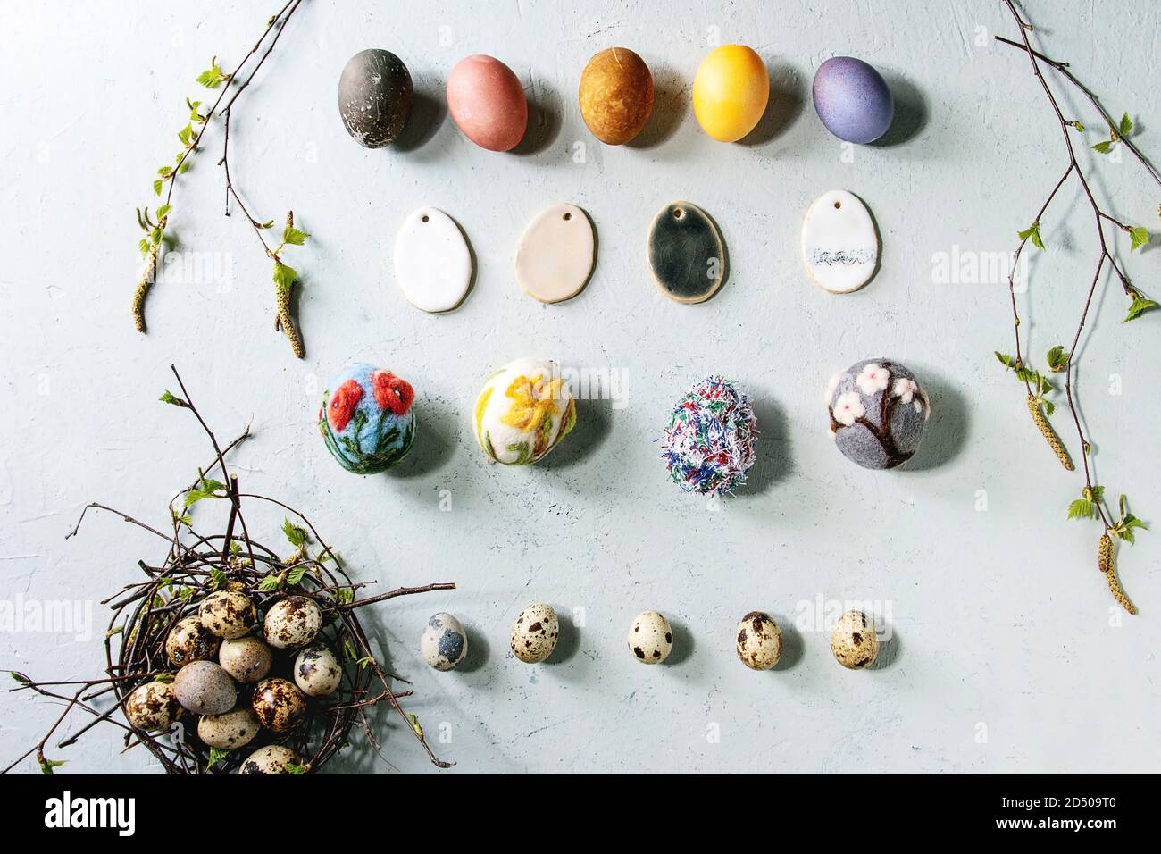 Bunte Huhn und Wachteleier in Birds Nest, handgemachtes Handwerk Wolle gefilzt und Keramik Eier in der Zeile, birke Niederlassungen über Hellgrau Textur Hintergrund. F Stockfoto