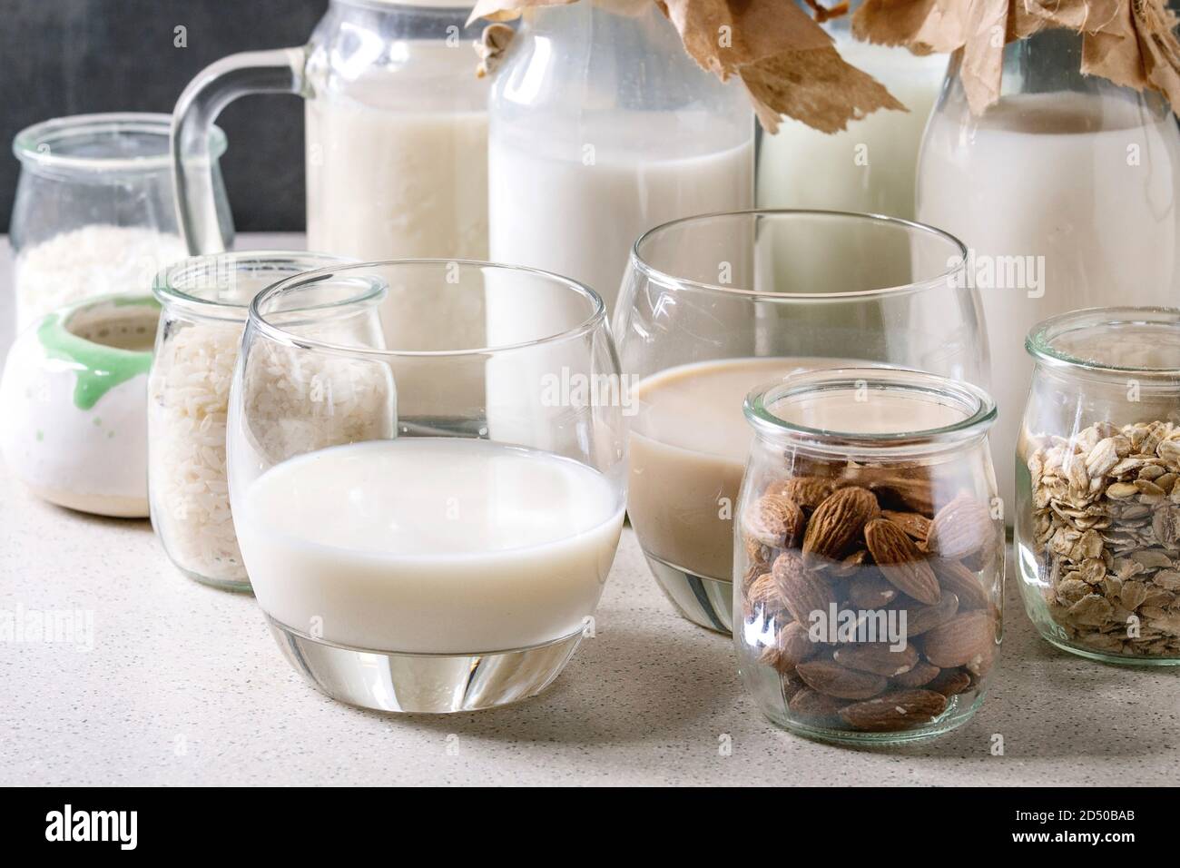 Vielzahl von Nicht-Milchprodukte vegan laktosefrei Nüssen und Getreide, Milch, Mandeln, Haselnuss, Kokos, Reis, Hafer in Glasflaschen mit Zutaten oben auf weißem Tabl Stockfoto