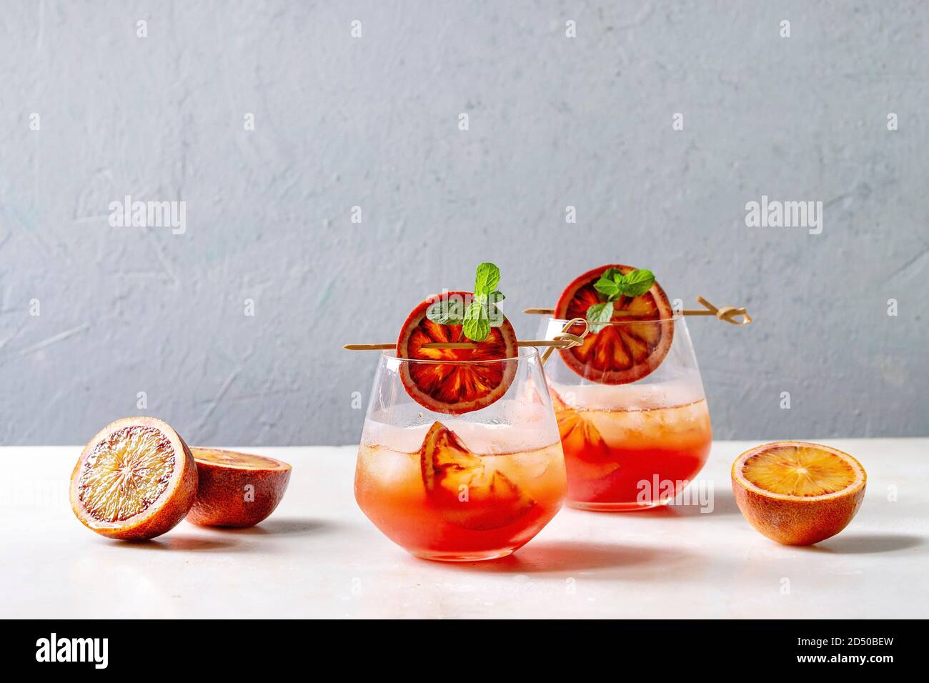 Blutorange Eistee Cocktails in Gläser, durch die Scheibe der Orangen und frischer Minze auf spieße eingerichtet, auf weissem Marmor tisch mit grauen Wand diente an Backgr Stockfoto