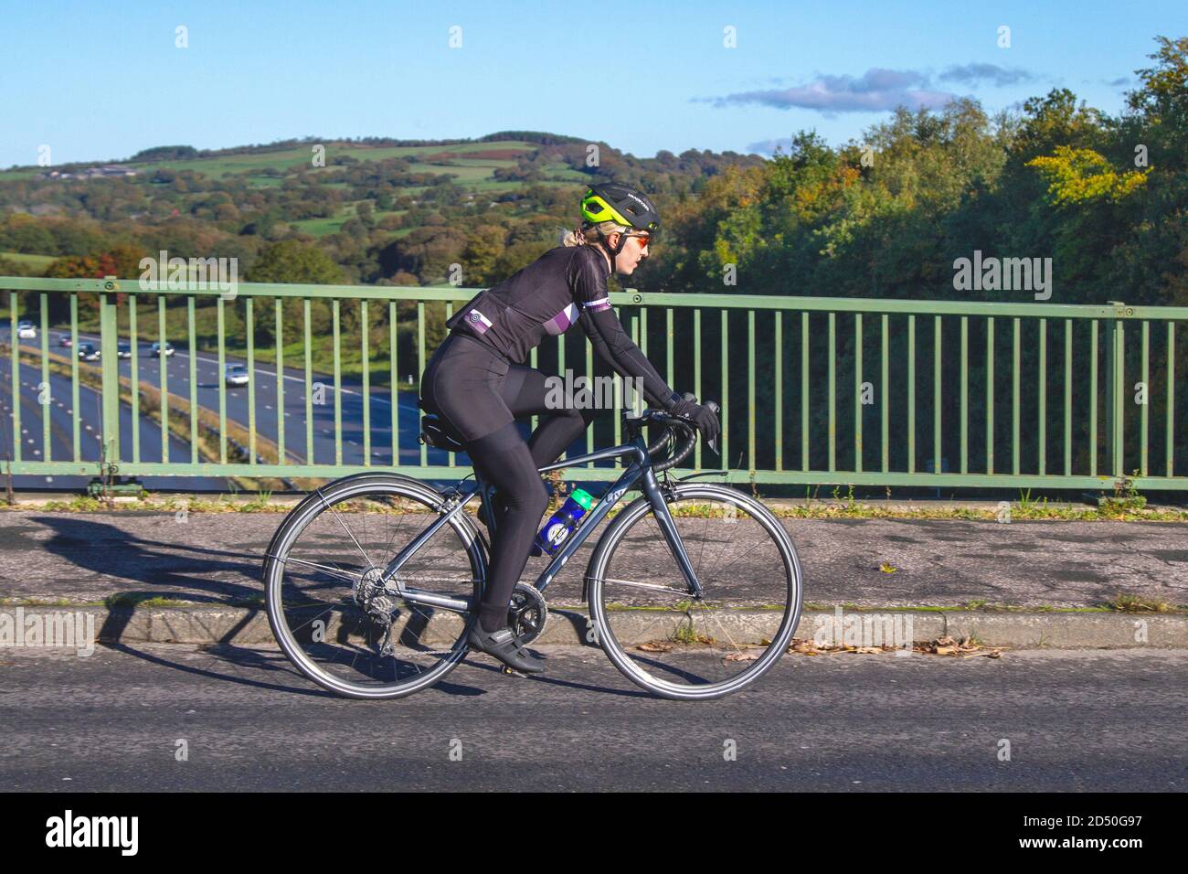 Radfahrerin in Lycra Reiten LIV Sport Rennrad auf dem Land Route Überqueren Autobahnbrücke im ländlichen Lancashire, Großbritannien Stockfoto