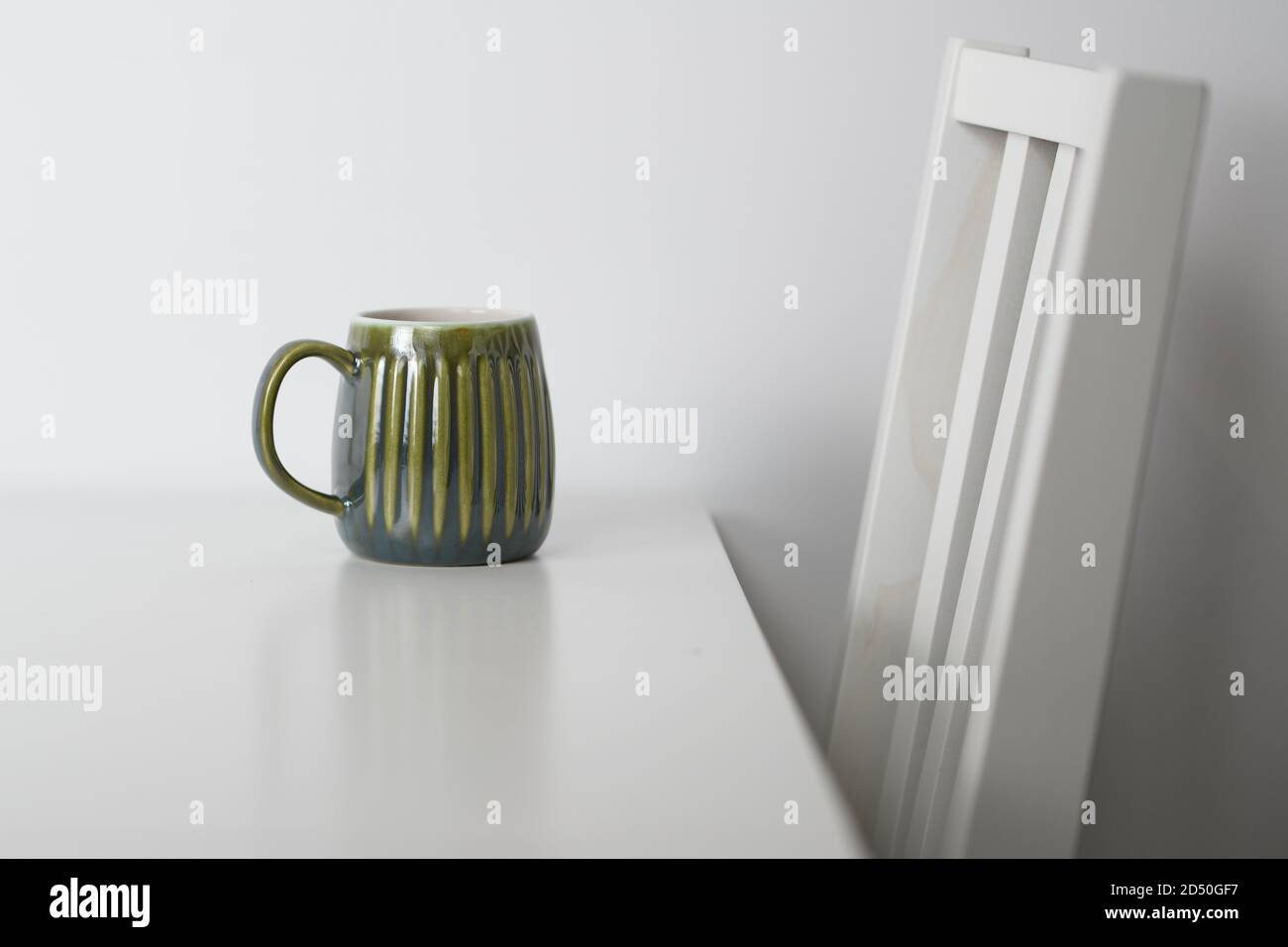 Grüner Becher auf einem weißen Tisch und einem weißen Stuhl Stockfoto