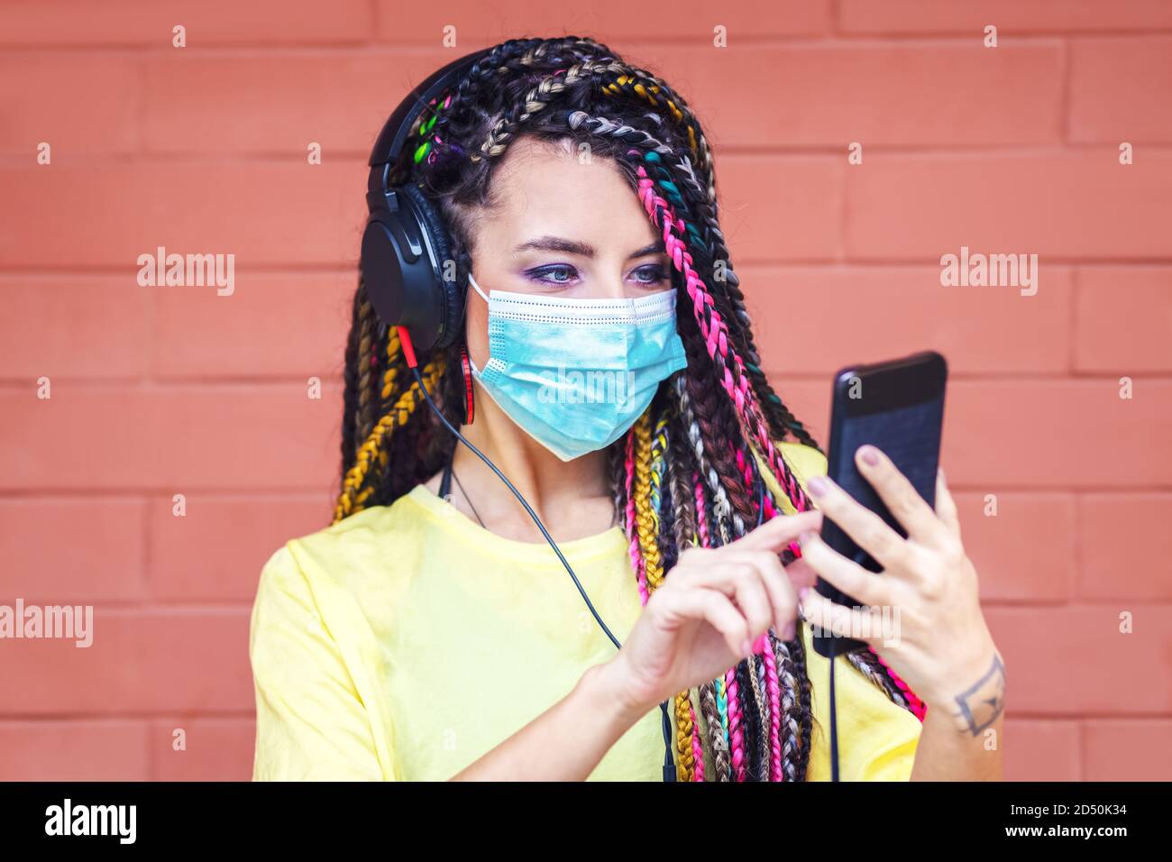 Junge Mixed-Race-Mädchen mit Dreadlocks Musik auf Kopfhörer hören Beim Tragen einer Gesichtsmaske Stockfoto