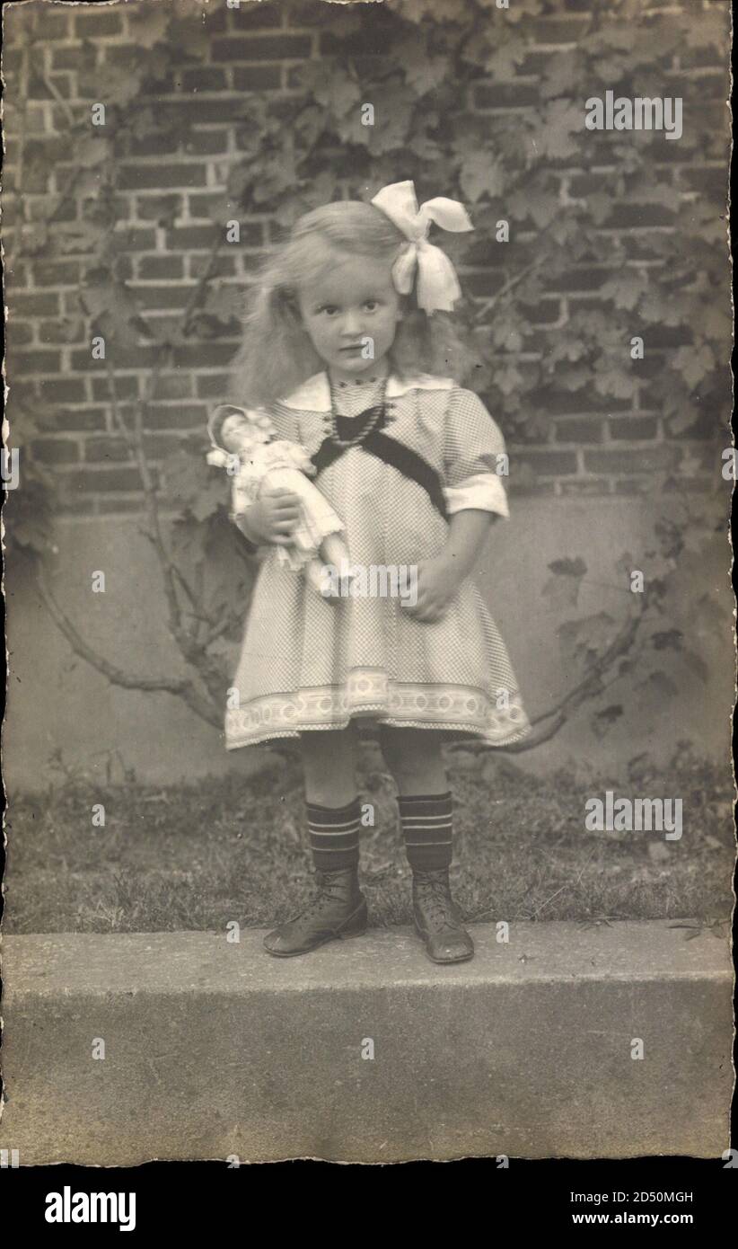 Kleines Mädchen in weißem Kleid, Haarschleife, Puppe, Spielzeug Stockfoto