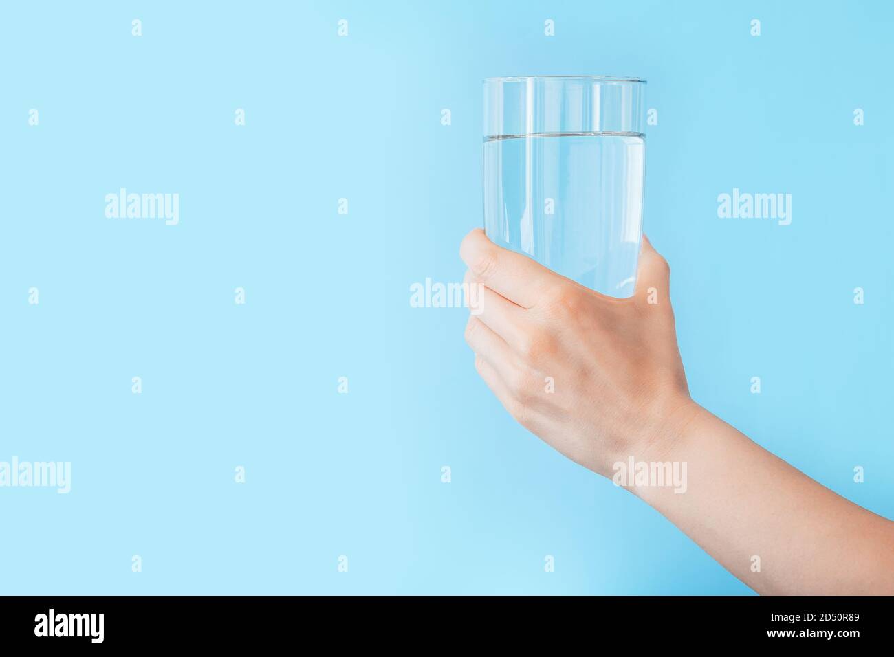 Wasserglas in weiblicher Hand auf blauem Hintergrund mit Kopierraum. Gesunder Lebensstil und Fitness-Konzept. Stockfoto
