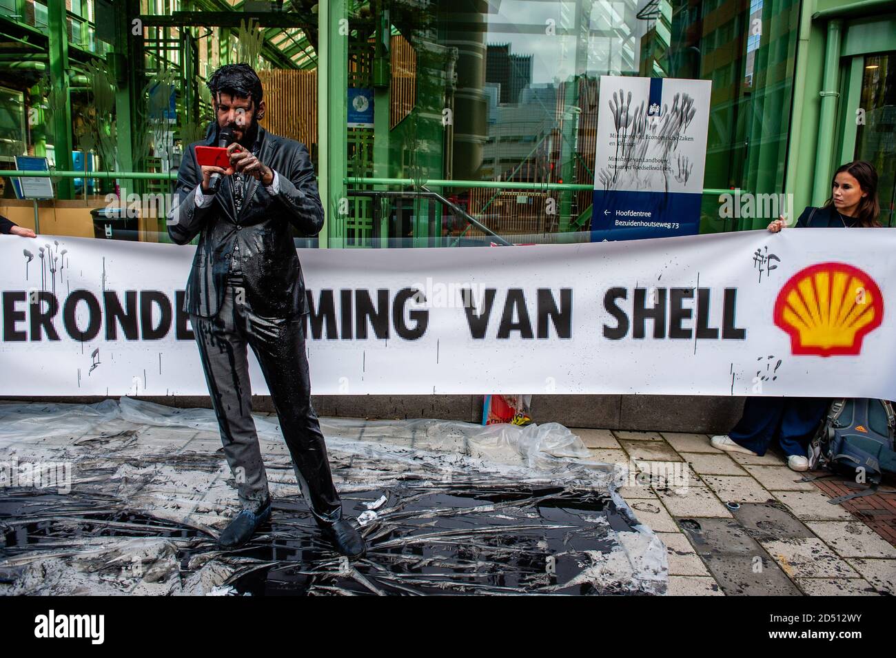 Ein Klimaaktivist, der eine Erklärung liest, während er mit gefälschtem Öl bedeckt ist.das Wirtschaftsministerium (EZK) organisiert einen Klimatag mit dem Ziel, die Niederlande mit "Spitzenreitern" zu inspirieren, die Treibhausgasemissionen bis 2030 zu halbieren. Verschiedene Klimagruppen protestieren gegen die Teilnahme von Marjan van Loon, Direktor von Shell Netherlands. Im Eröffnungspanel des Klimatages. Mehrere Klimaorganisationen tauchten vor dem Gebäude des Ministeriums für Wirtschaft und Klimapolitik in Den Haag gegen Shell als Ehrengast am "Klimatag" auf. Die Klimaaktivisten wir Stockfoto