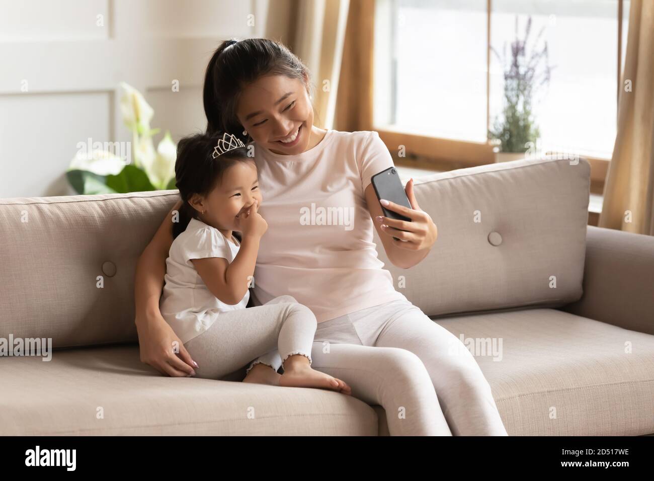 Lachende asiatische Mutter und kleine Tochter umarmt, mit Telefon zusammen Stockfoto