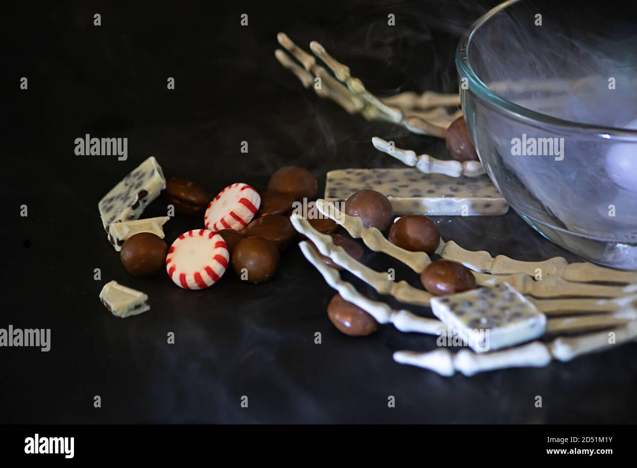 Skeletthänden mit verschütteten Pralinen und Bonbons auf einem schwarzen Hintergrund Stockfoto