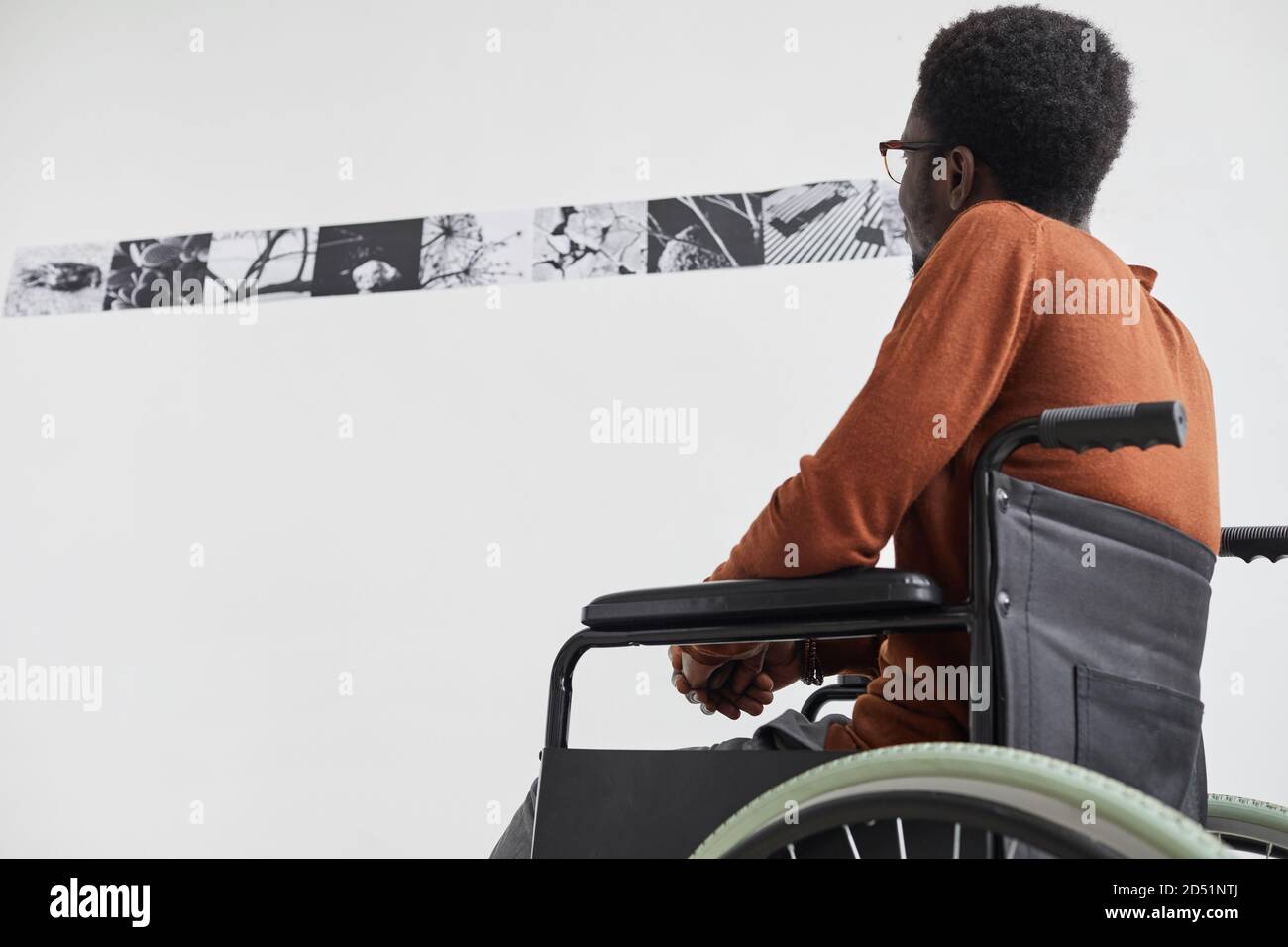 Grafisches Porträt eines jungen afroamerikanischen Mannes mit Rollstuhl und Blick auf Gemälde während der Erkundung der modernen Kunstgalerie Ausstellung, copy space Stockfoto