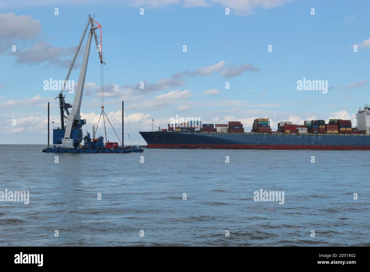 Ein Arbeitsschiff und ein Containerschiff, das bei Flut an der Elbmündung vorbeifährt. Hier mündet die Elbe in die Nordsee. Cuxhaven, Deutschland. Stockfoto