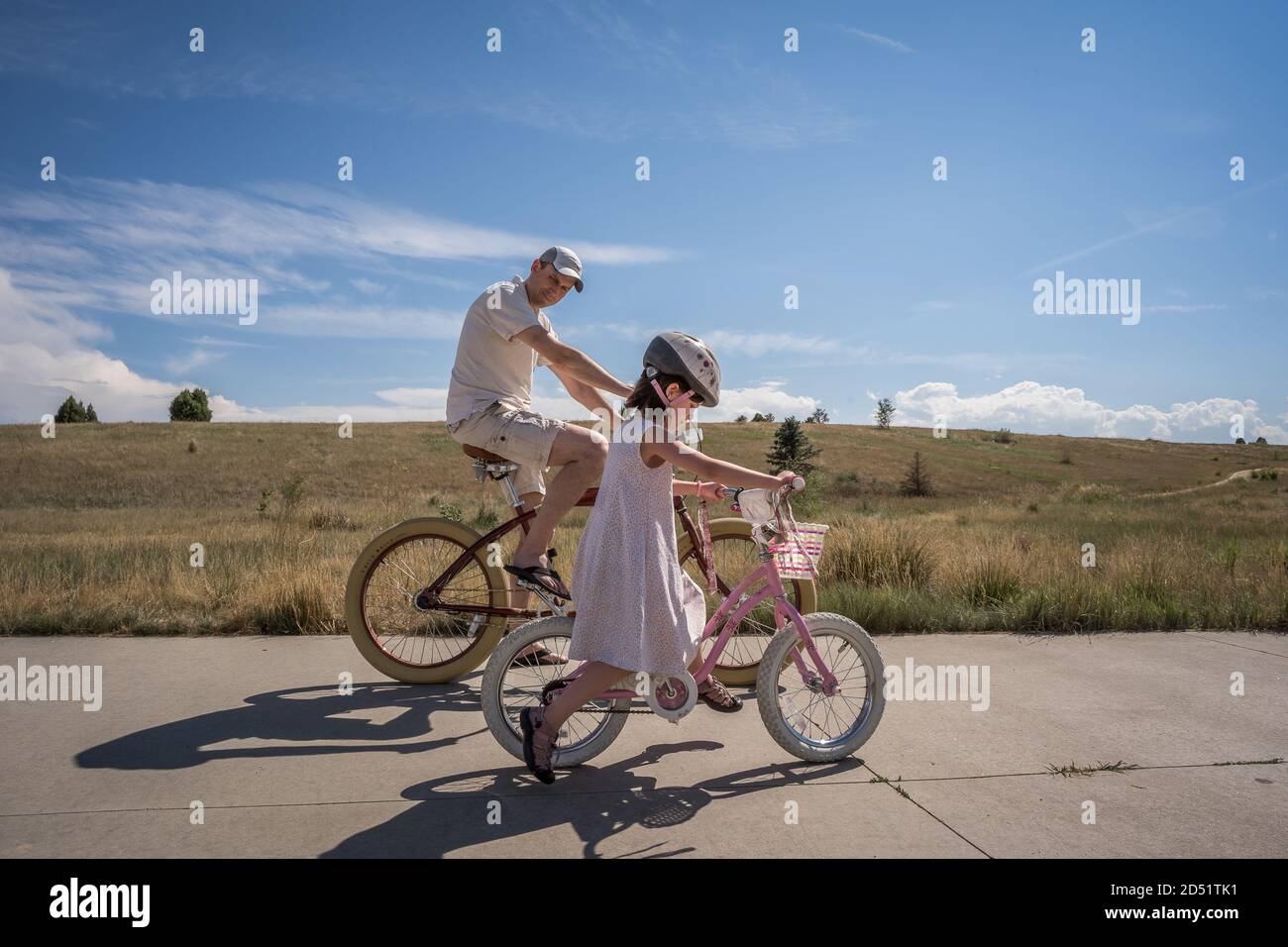 Papa schaut zu Tochter, als sie lernt, ein zu reiten Fahrrad ohne Trainer Stockfoto