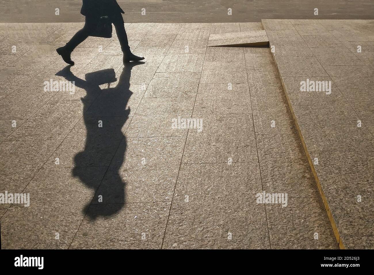 Silhouette eines Mädchens auf dem Hintergrund einer Stadtstraße. Ein großer Schatten einer Frau, die mit einer Tasche geht. Eine Frau in Eile auf ihrem Geschäft. Stockfoto