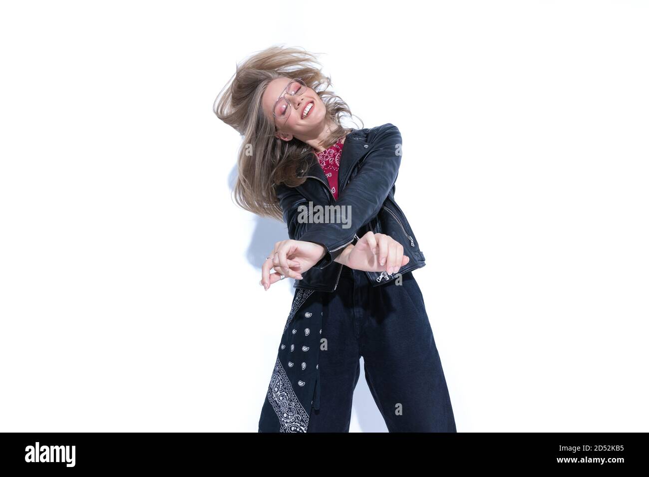 Fröhliche Mode-Modell hält Hand gekreuzt und tanzen, trägt Brille und Lederjacke auf weißem Studio Hintergrund Stockfoto