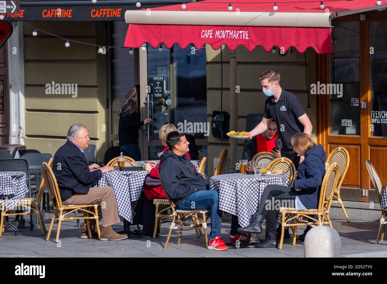 Kellner mit Maske serviert Essen am Tisch in einer Outdoor-Bar, Café oder Restaurant während Covid oder Coronavirus Ausbruch, zweite Welle Stockfoto