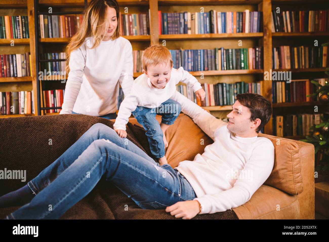 Familienportrait zu Weihnachten. Junge kaukasische Familie in identischer  Kleidung Spaß auf dem Sofa im Wohnzimmer mit großer Bibliothek von Büchern  und Weihnachten Stockfotografie - Alamy
