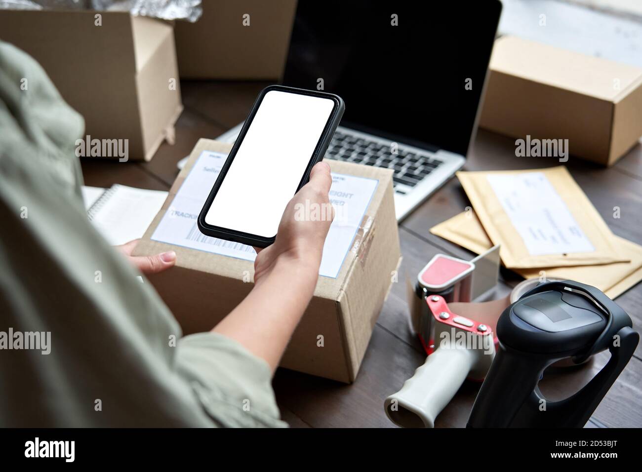 Weibliche Lagerarbeiterin, die den Paketkasten über eine mobile Anwendung hält. Stockfoto