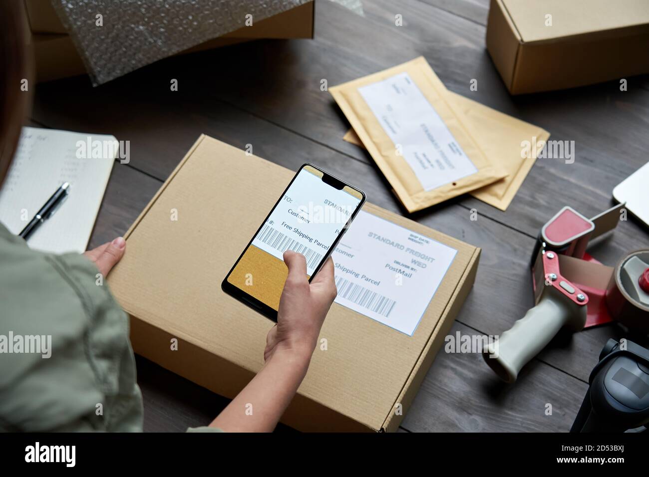 Weibliche Lagerarbeiterin scannt Barcode auf Versandkarton auf dem Smartphone. Stockfoto