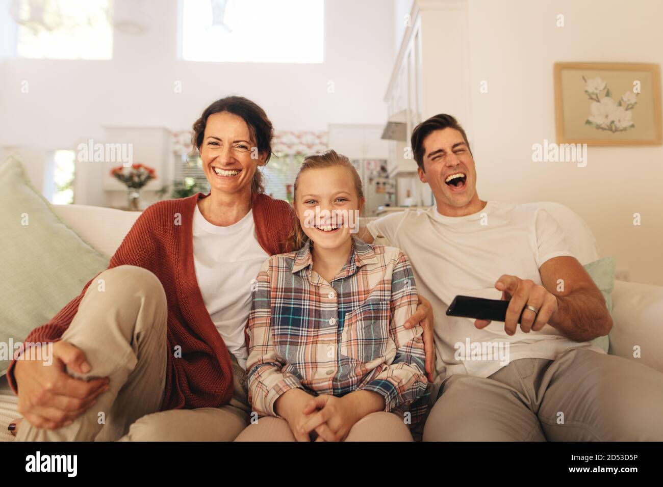 Familie schaut Comedy-Film im Fernsehen zu Hause. Vater, Mutter und Tochter sitzen zu Hause beim Fernsehen und lachen. Stockfoto
