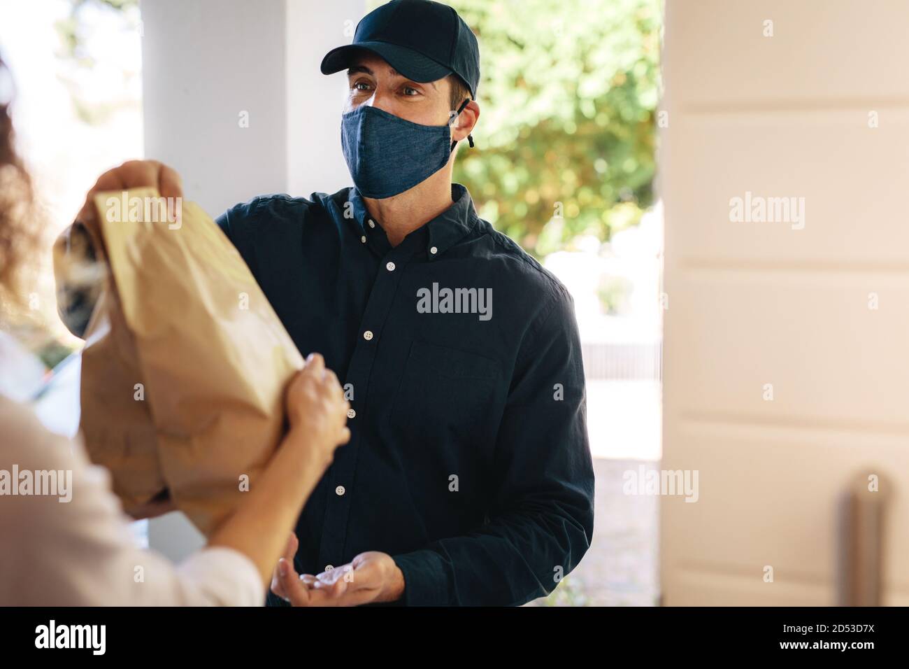Delivery Mann mit Gesichtsmaske Lieferung Pakete an eine Frau zu Hause. Lieferservice während einer Corona-Virus-Pandemie. Stockfoto