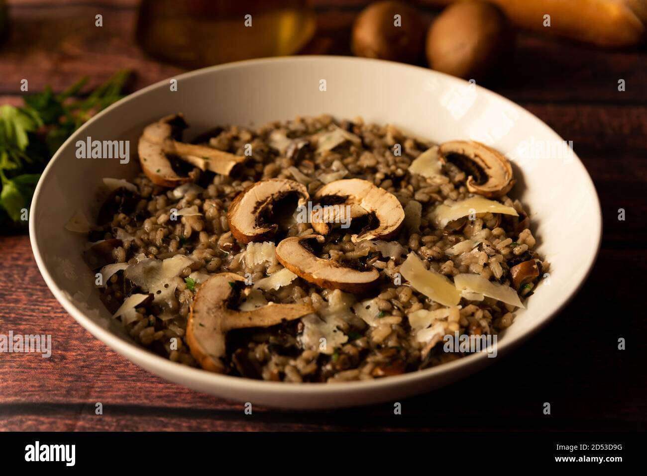 Risotto mit Pilzen, italienische Küche, bekannt als Risotto ai funghi, Nahaufnahme mit warmem Licht, Petersilie, Seitenansicht, auf dunkelbraunem Holztisch. parmesan-Flocken Stockfoto