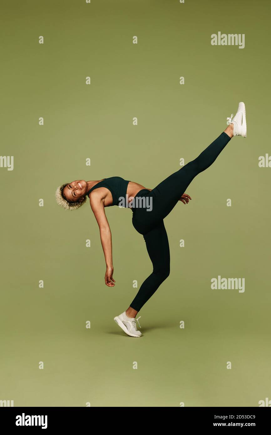 Lächelnde afroamerikanische Frau tut extreme Beinstrecken balancieren auf einem Bein. Weibliche Sportlerin beim Training an Beweglichkeit Übungen. Stockfoto