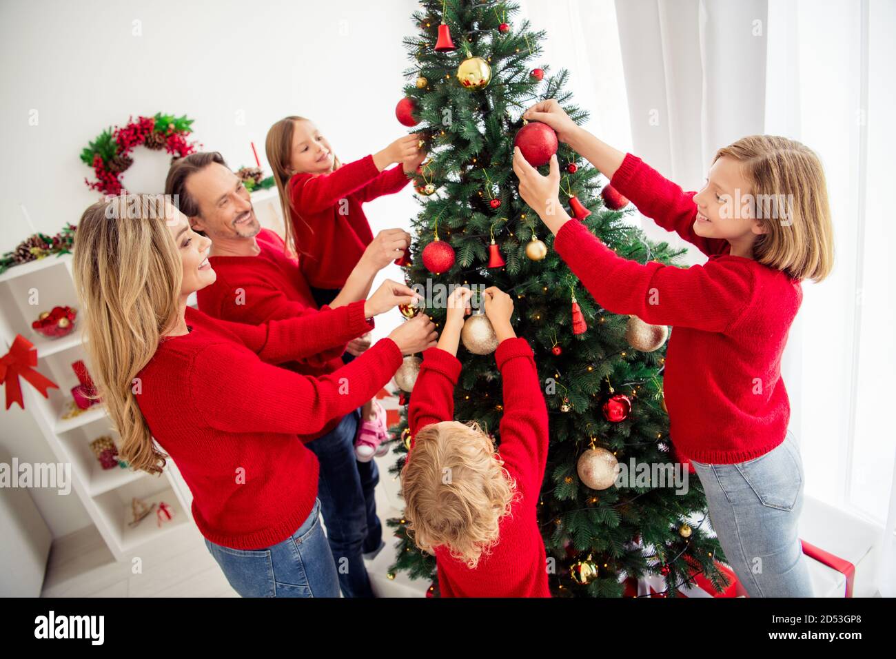 Foto der ganzen großen Familie fünf Menschen sammeln Liebhaber Eltern Drei kleine Kinder schmücken Weihnachtsbaum halten Bälle Papa Hilfe Die Beleuchtung der Tochter trägt einen roten Pullover Stockfoto