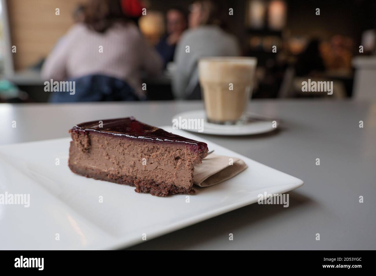 Ausgewählte Fokus Blick auf einfach Schokolade Käse Kuchen auf weißem Teller neben mit einer Tasse Kaffee, auf dem Tisch neben Fenster des hellen Cafés. Stockfoto