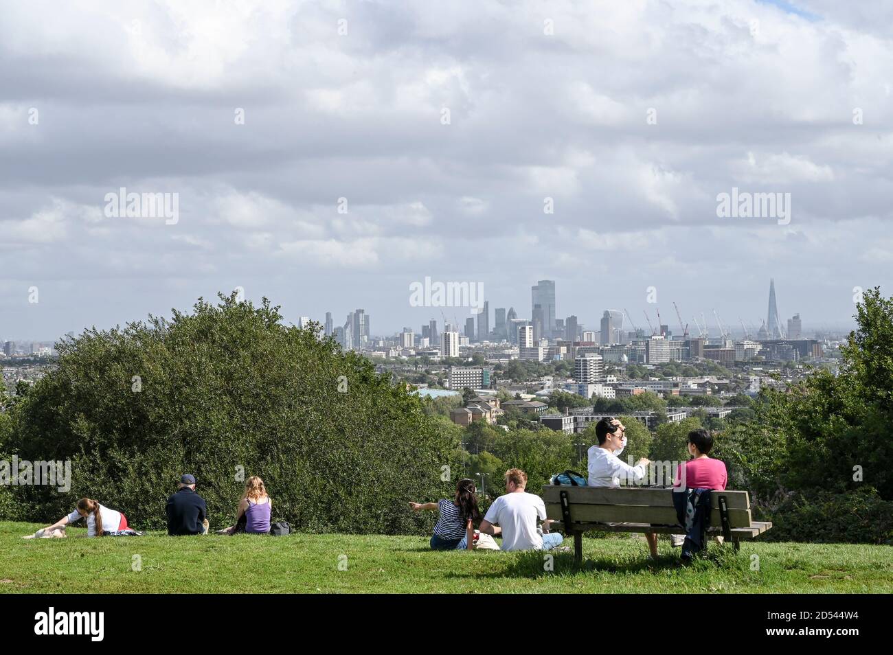 Menschen unterhalten sich in kleinen Gruppen auf Parliament Hill, London, Großbritannien, mit Blick auf London City Sky Line. Stockfoto