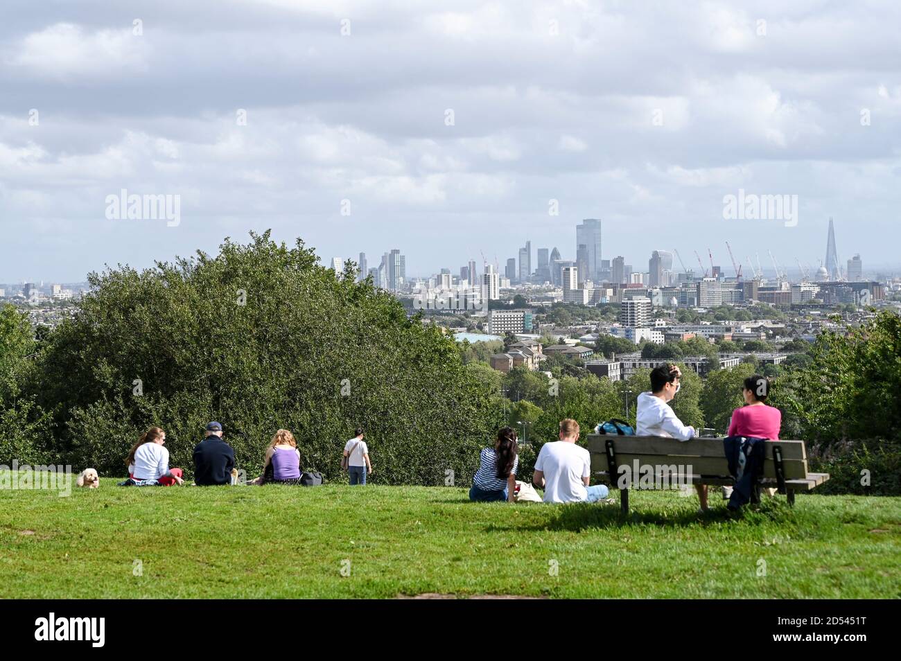 Menschen unterhalten sich in kleinen Gruppen auf Parliament Hill, London, Großbritannien, mit Blick auf London City Sky Line. Stockfoto