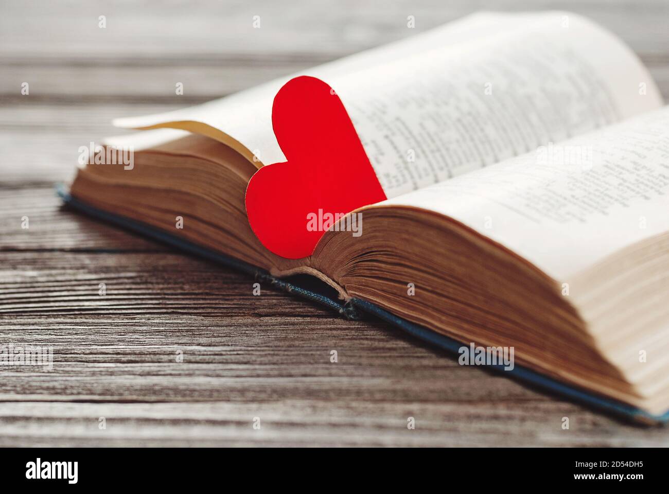 Offenes Buch mit rotem herzförmigem Papierlesezeichen auf Holz Hintergrund Stockfoto