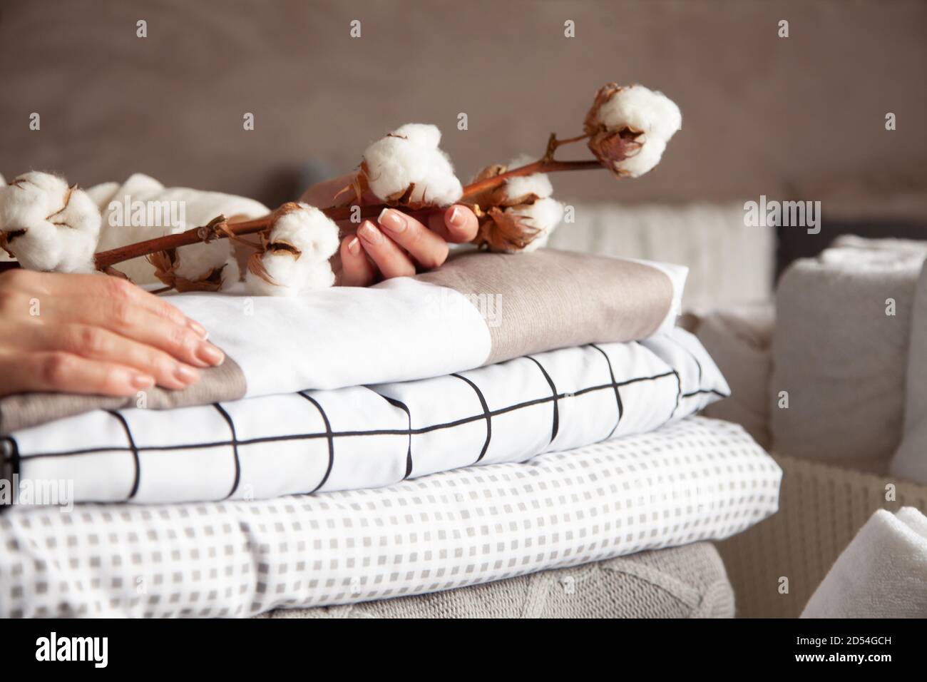 Gut gepflegte Frau Hände halten die Baumwollzweig mit Haufen Von gefalteten Bettlaken und Decken Stockfoto