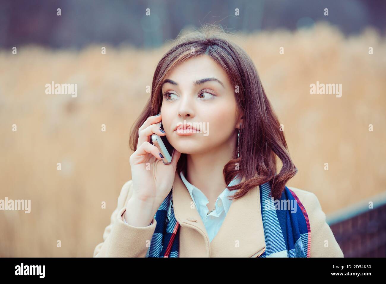 Skeptische Frau am Telefon zu entscheiden, was im Freien zu beantworten park im Herbst auf dem Hintergrund Stockfoto