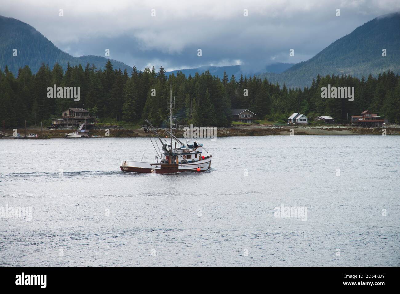 Fischerboot, das seinen Weg aus dem Hafen mit Bergen und Pinien im Hintergrund macht. Stockfoto