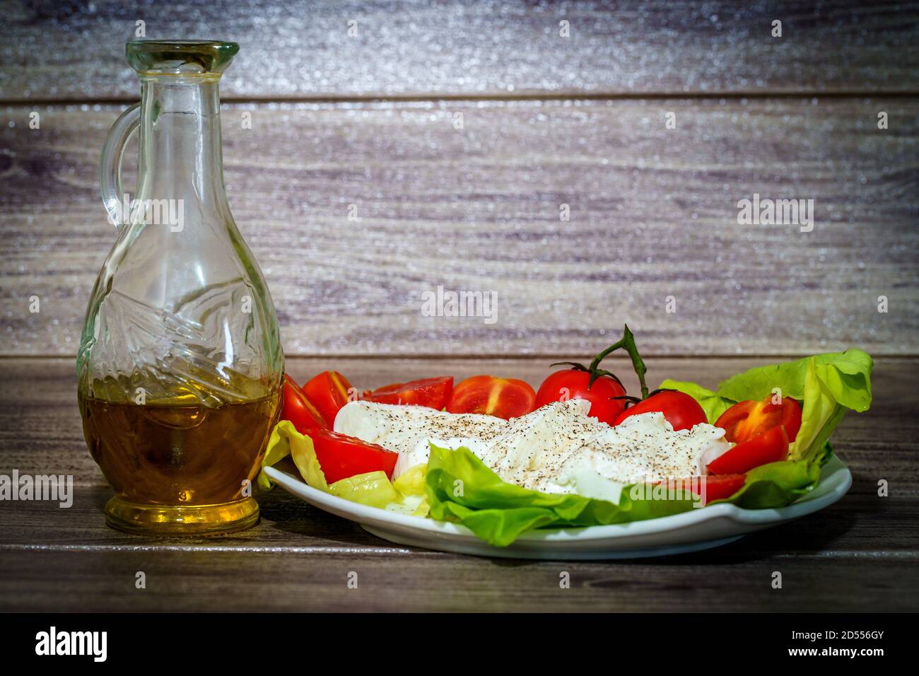 Italienischer Büffelmozzarella-Käse mit Kirschtomaten und nativem Olivenöl extra auf grünen Salatblättern serviert. Stockfoto