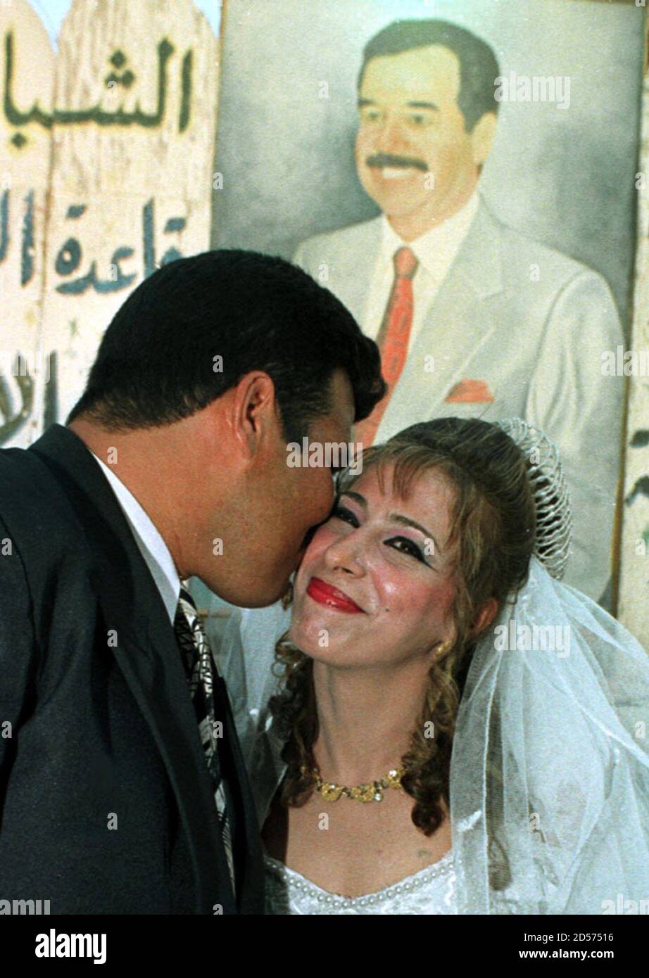 Eine Frisch Verheiratete Braut Und Ein Brautigam Kussen Sich Vor Einem Portrat Von Saddam Hussein Nach Einer Massenhochzeit In Bagdad Am 9 August Rund 112 Paare Heirateten Am Montag Bei Einer Veranstaltung