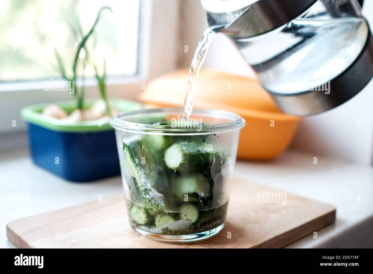 Gieße Wasser aus einem Wasserkocher in ein Glas Gurken. Vorbereitung auf den Winter. Stockfoto