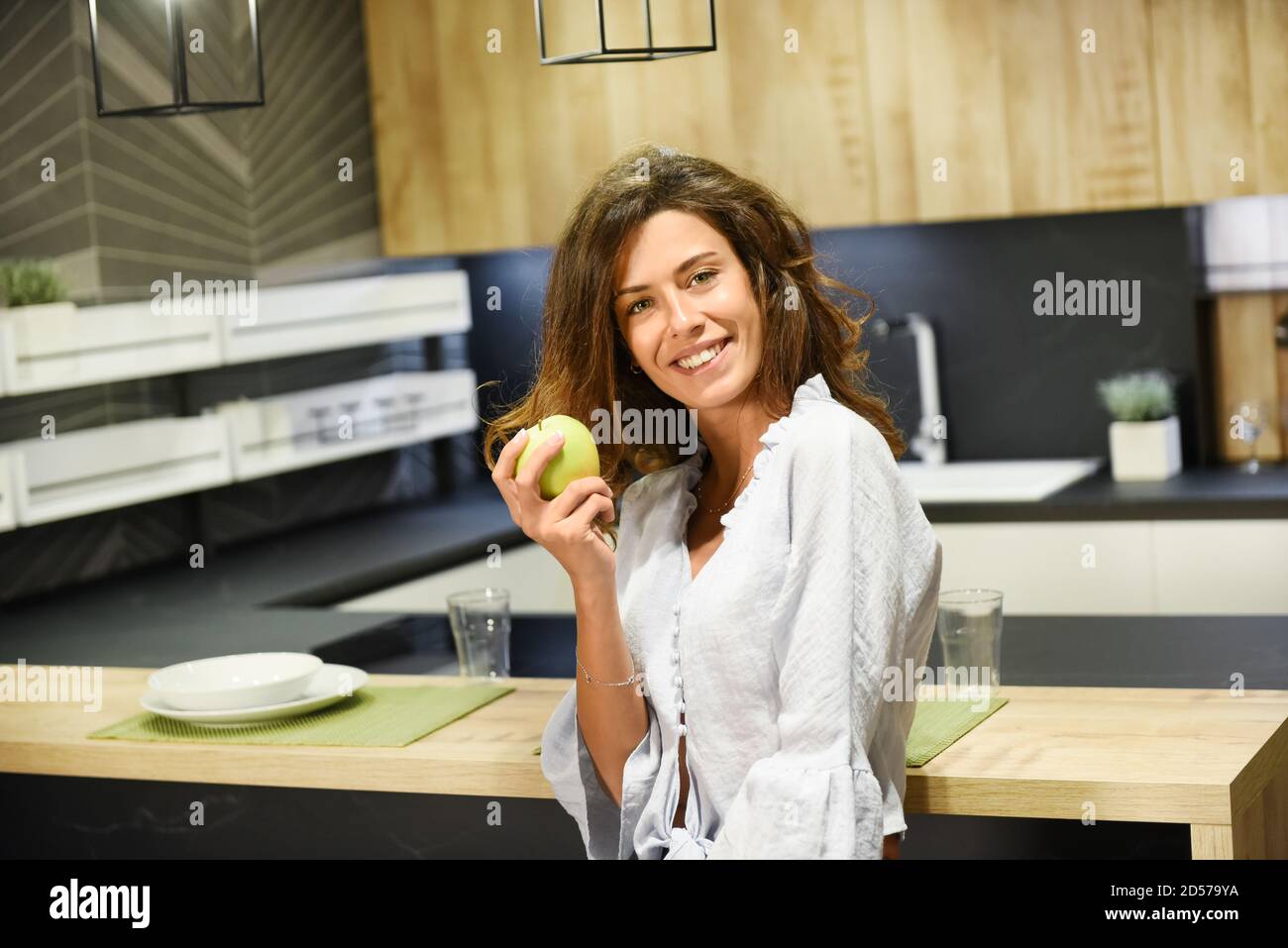 Lächelnd lebhaft Frau hält einen frischen grünen Apfel in ihr Offene Küche in einem Konzept für eine gesunde Ernährung Und Ernährung Stockfoto