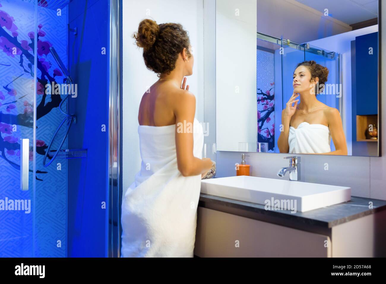 Attraktive junge Frau bewundert ihre Reflexion im Badezimmerspiegel Während eingewickelt in ein sauberes weißes Handtuch nach der Einnahme ein Dusche in einer persönlichen Hygiene Stockfoto