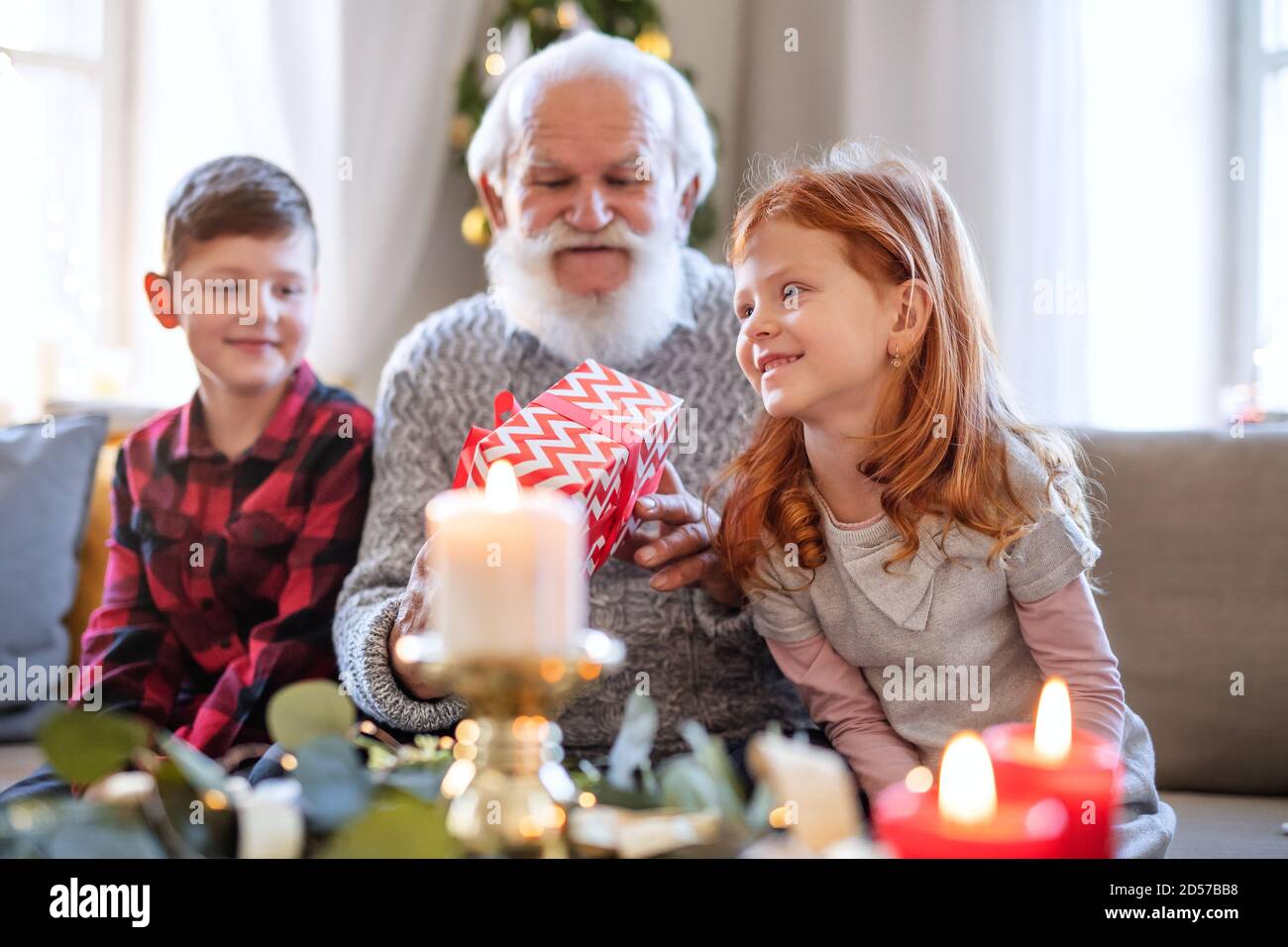 Kleine Kinder mit Senioren Großvater drinnen zu Hause zu Weihnachten, hält Geschenke. Stockfoto