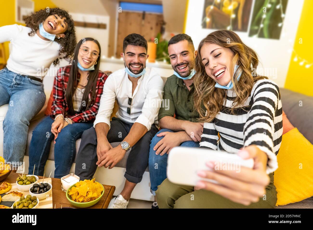 Eine Gruppe gemischter Rennfreunde, die zu Hause Selfie feiern Mit medizinischer Schutzmaske - Happy People Indoor Aperitif Party Am Coronavirus neu Stockfoto